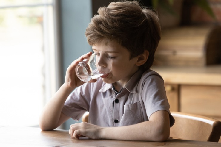 Una bambino beve dell'acqua da un bicchiere