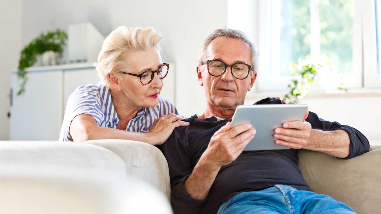 Due pensionati in soggiorno leggono su un tablet